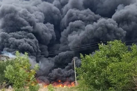 Густа чорна хмара диму над пожежею біля промислової споруди та дерев