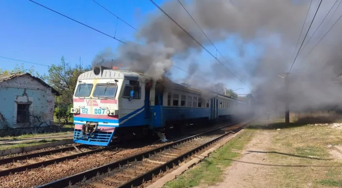 Електричка УЗ з димом біля будівлі на коліях під синім небом