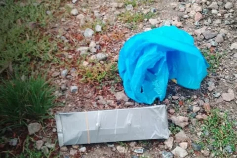 Зім’ятий синій пакет і обмотаний стрічкою сірий прямокутник на гравії