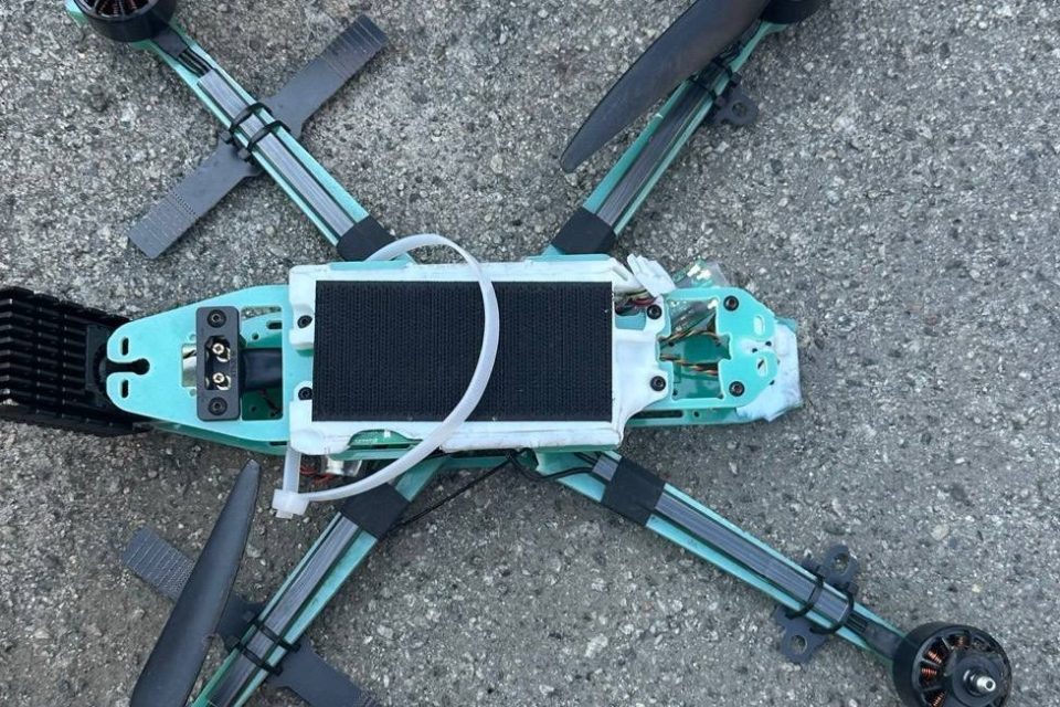 Бірюзовий FPV-дрон з акумулятором і пропелерами лежить на асфальті